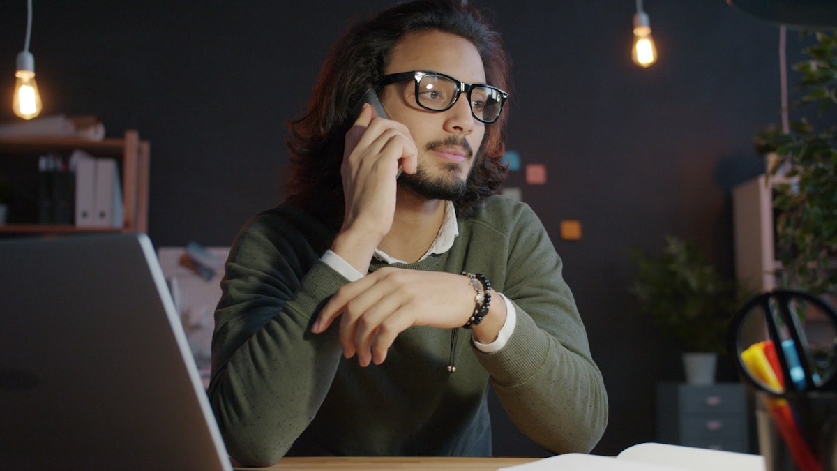 A business owner on a phone call at his desk next to his laptop